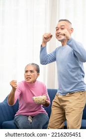 Excited Mature Couple, Senior Man And Woman Watching Tv, Senior Sport Fans Celebrating Favorite Team Victory, Sitting On Cozy Couch And Eating Popcorn Snack At Home, Enjoying Weekend. Happy Senior.