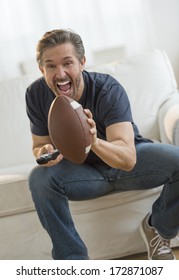 Excited Mature Man Cheering While Watching American Football Match On Sofa