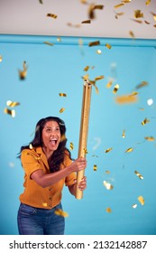 Excited Mature Woman Celebrates Winning Firing Gold Confetti Canon In Studio Against Blue Background