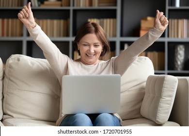 Excited Mature Woman Looking At Laptop Screen, Reading Good News In Message, Celebrating Online Lottery Win, Rejoicing Success, Overjoyed Older Female Sitting On Couch At Home, Using Computer