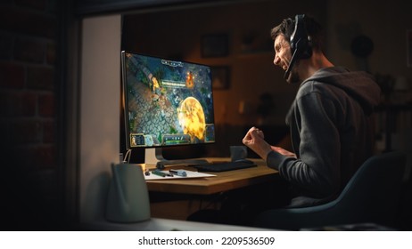 Excited Middle Aged Male Gamer Playing Online Video Game On Personal Computer. Guy Enjoying Fantasy RPG Game With Role Playing Character Casting Spells, Destroy Enemies. Shot From Outdoors.