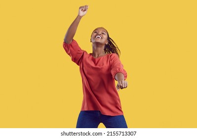 Excited millennial African American girl isolated on yellow studio background dancing listening to music. Smiling young black woman have fun make dancer moves Gangnam style. Entertainment.