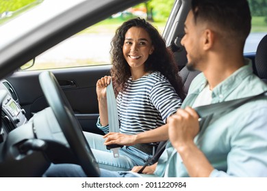 Excited Millennial Arab Couple Fastening Seat Belt, Looking At Each Other And Smiling, Going Vacation By Car, Side View, Closeup. Mixed Race Young Family Having Weekend Trip, Enjoying Nice Weather