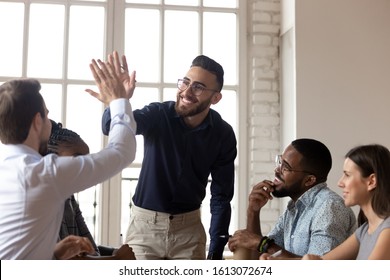 Excited millennial Arabic businessman give high five to Caucasian male colleagues at meeting, smiling multiethnic businesspeople join hands celebrate business success in office, cooperation concept