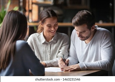Excited millennial couple meeting with female realtor or broker in cafe sign contract buying first property together, happy spouses put signature on agreement close deal with banker take loan