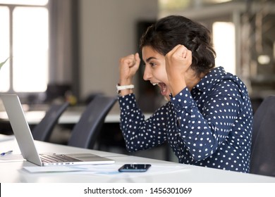 Excited Millennial Employee Sit At Desk Witness Online Lottery Win On Laptop, Scream From Happiness, Happy Indian Woman Winner Look At Computer Screen Hit Jackpot, Female Office Worker Read Good News