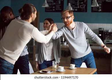 Excited Millennial Friends Greeting, Hanging Together In Café, Smiling Guy Get Acquainted With Colleague At Friendly Meeting In Coffeeshop, Diverse Students Reunited In Cafeteria Embracing Say Hello