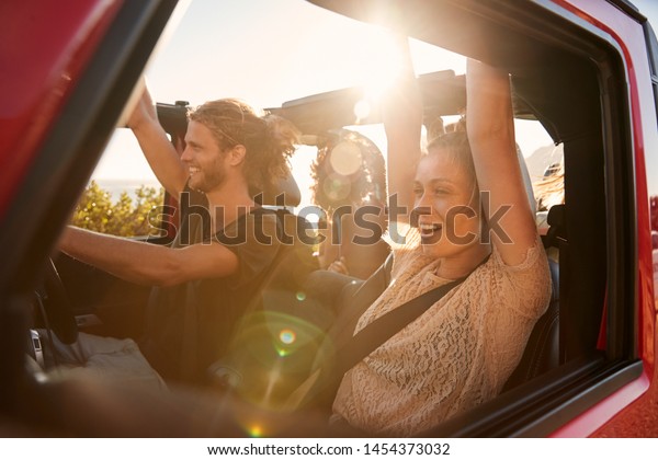 Excited millennial friends on a road\
trip vacation driving in an open car, close up, lens\
flare