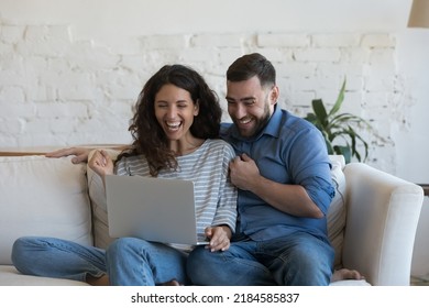 Excited millennial married couple looking at laptop computer screen with winner yes hands, laughing, shouting for joy, celebrating success, achieve, winning prize, money, learning good happy news - Powered by Shutterstock