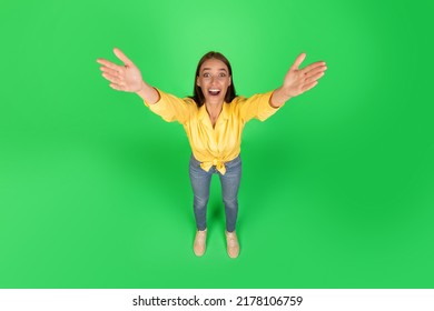 Excited Millennial Woman Stretching Arms Smiling To Camera Taking Something Posing Standing Over Green Studio Background. Give Me This Concept. High Angle Shot