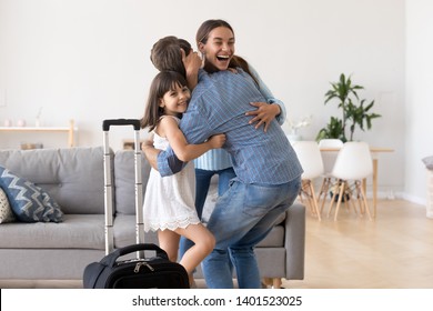 Excited Mom And Cute Little Daughter Hug Happy To See Dad Come Home With Baggage From Business Trip, Smiling Overjoyed Family Embrace In Living Room Reunited, Mother And Child Welcome Father