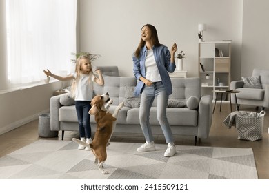 Excited mom and happy preschool daughter kid dancing with playful pet, hopping in living room, having fun, laughing, enjoying active leisure, music at home, training adorable beagle dog. Full length - Powered by Shutterstock