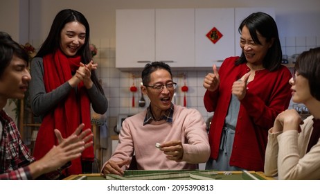 excited mother and daughter cheering and massaging the father as he wins by his own draw on mahjong gambling table. chinese text at background translation: luck