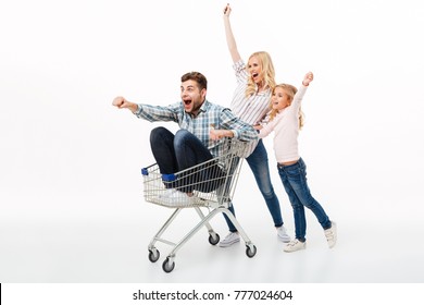 Excited Mother And Her Daughter Giving A Ride On A Shopping Trolley To Their Father Isolated Over White Background