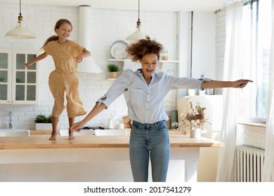 Excited Mother And Little Daughter Dancing On Table To Favorite Music In Modern Kitchen Together, Happy Mom With Adorable Kid Girl Having Fun, Family Engaged In Funny Activity, Enjoying Leisure Time