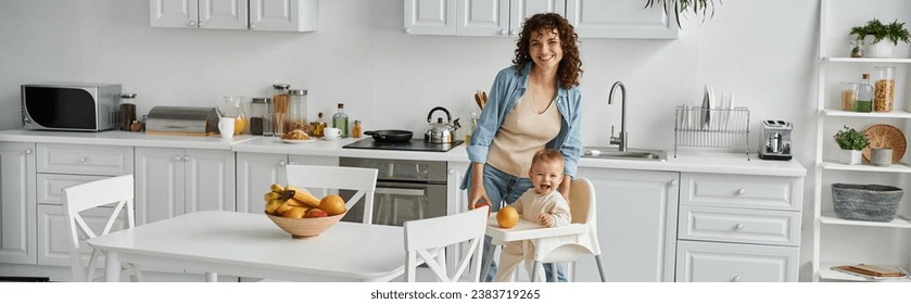 excited mother and toddler daughter looking at camera near fresh fruits in modern kitchen, banner - Powered by Shutterstock