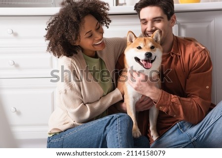 excited multiethic couple hugging shiba inu dog in kitchen