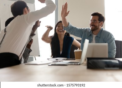 Excited Multi-ethnic Business People Group Sit At Desk In Modern Boardroom Raising Hands Giving High Five Celebrating Closing Profitable Deal, Found Investors, Sales Growth, Unity Team Spirit Concept