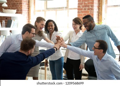 Excited multiracial colleagues give high five involved in teambuilding activity at meeting, happy diverse workers join hands celebrate success or win, show team spirit and unity. Cooperation concept