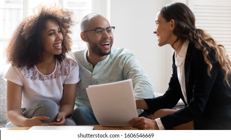 Excited multiracial young couple visit smiling female consultant talk buying first home together, happy international millennial husband and wife speak consulting with woman lawyer or broker