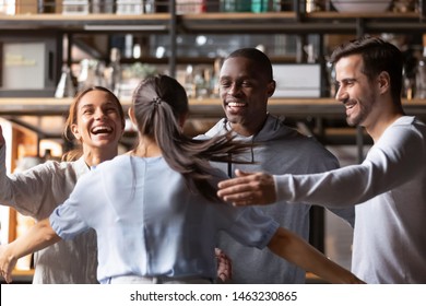 Excited Multiracial Young People Hanging Out Together In Cafe Meeting New Girlfriend Giving Hug, Happy Diverse Friends Feel Overjoyed Welcoming Colleague Relaxing Having Fun In Bar Or Restaurant