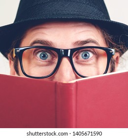 Excited Nerd Hiding Behind Books. Playful Happy Young Man In Funny Glasses And Vintage Hat Holding A Book. Nerd Hipster Guy In Hat. Never Too Late To Study. Amazing Man Has Great Idea