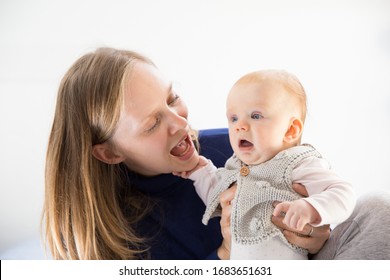 Excited new mom talking to her cute little baby girl. Young woman nursing six month daughter in bedroom at home. Motherhood concept
