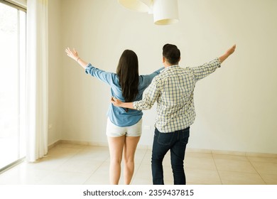 Excited newlyweds couple seen from behind celebrating getting their new house or apartment together and hugging