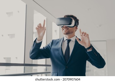 Excited office worker in vr headset or virtual reality goggles gesturing with hands, using innovative technologies for business at work, dressed in suit, smiling and touching objects in digital world - Powered by Shutterstock