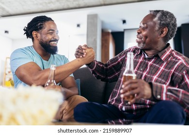 Excited old father and son watching tv,drink beer, having fun at home