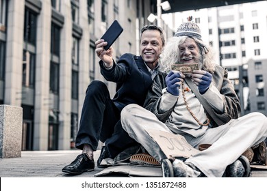 Excited Old Homeless. Vain Rich Man In Costume Making Selfie Of Donation Money To Desperate Poor Man