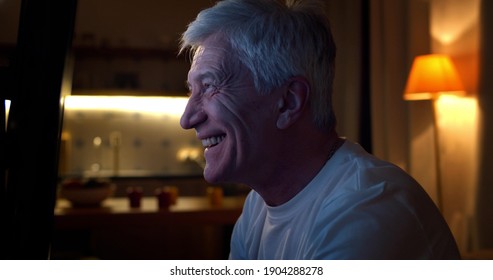 Excited Old Man Watching Football Match On Tv Late In Evening. Side View Of Happy Senior Make Sitting Near Tv Screen And Celebrating Favorite Sports Team Victory