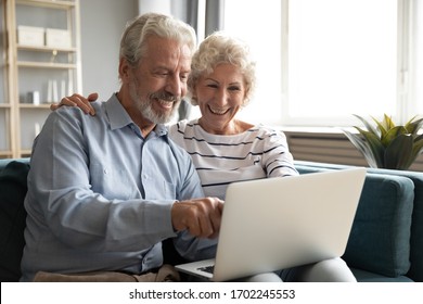 Excited Older Couple Reading Good News On Social Network Or Email, Using Laptop Together, Mature Man And Woman Chatting Or Shopping Online, Browsing Banking Service, Sitting On Couch At Home