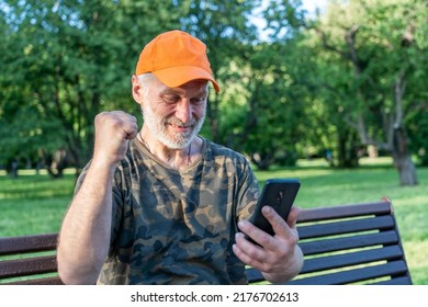 Excited Older Man Winner Holding Smartphone And Online Bet Bid Game Win At Park Bench, Happy Senior Male Looking At Cell Phone Shouting For Joy, Getting Good News, Making Winner Yes Hand Gesture.