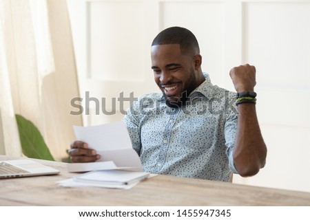 Excited overjoyed african business man student winner read postal mail letter happy with good news promotion scholarship, got new job celebrate salary rise payment taxes refund receive loan approval