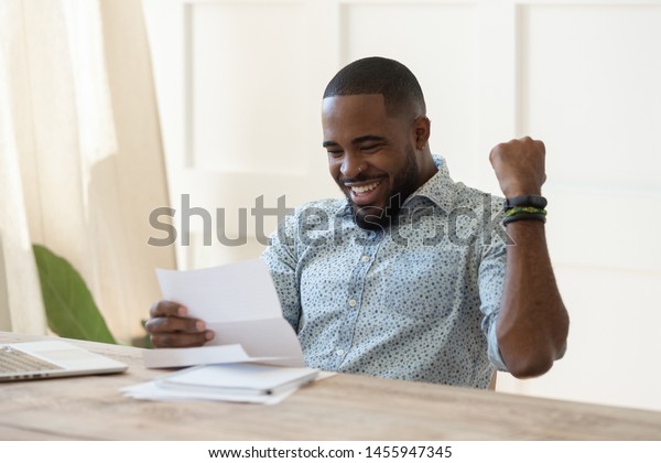 Excited overjoyed african business man student\
winner read postal mail letter happy with good news promotion\
scholarship, got new job celebrate salary rise payment taxes refund\
receive loan approval