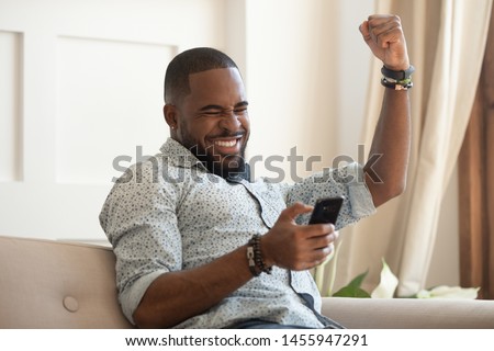 Excited overjoyed black man winner holding smartphone feeling euphoric with mobile online bet bid game win, happy ecstatic african guy looking at cell phone celebrate receiving reading good news