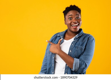 Excited Overweight African American Woman Pointing Finger Aside Advertising Text Standing Over Yellow Studio Background. Look There Advertisement Banner Concept. Copy Space