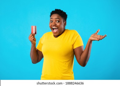 Excited Overweight African Lady Holding Credit Card Advertising Bank Service Standing Over Blue Background, Smiling To Camera. Finance And Money Concept. Studio Shot