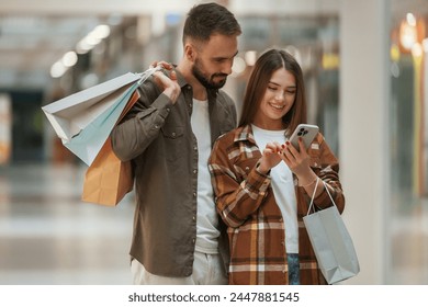 Excited people with smartphone. Young couple are in supermarket together. - Powered by Shutterstock