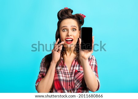 Excited pinup lady showing smartphone with blank screen, empty space for your website or mobile app design, blue studio background. Classy young woman showing cellphone with mockup