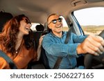 Excited playful European couple in sunglasses driving luxury car, enjoying music, singing and smiling, spouses going on vacation, windshield view