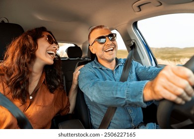 Excited playful European couple in sunglasses driving luxury car, enjoying music, singing and smiling, spouses going on vacation, windshield view - Powered by Shutterstock