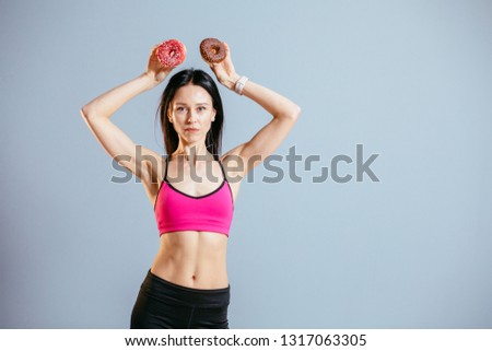 Excited playful sports woman in pink top holding fresh pink and chocolate donuts with powder ready to enjoy sweets. Portrait of attractive brunette slim female in having fun with sweet-stuff.  Copy space text.