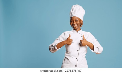 Excited positive woman giving thumbs up on camera, earing kitchen apron and expressing like or approval symbol. Professional restaurant chef showing agreement gesture and success. - Powered by Shutterstock