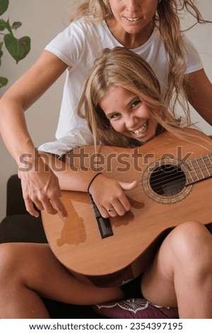 Excited positive young female with toothy smile sitting on sofa and playing acoustic wooden guitar while looking at camera