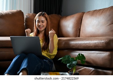 Excited And Pretty Millennial Asian Woman In The Living Room Using Laptop Computer To Check Her Job Offer Email.