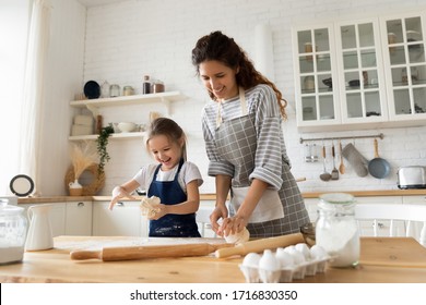 Excited pretty young woman in apron making homemade pastry with cute small child daughter. Smiling little preschool girl playing with dough, enjoying cooking process with happy mother in kitchen. - Powered by Shutterstock