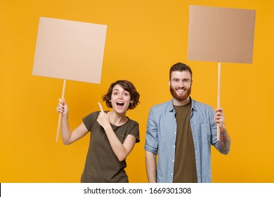 Excited protesting two people guy girl pointing index finger on protest signs broadsheet blank placard on stick isolated on yellow background. Protests strikes pickets concept. Youth against city