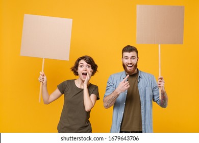 Excited protesting young two people guy girl hold protest signs broadsheet blank placard on stick isolated on yellow background studio portrait. Protests strikes pickets concept. Youth against city.